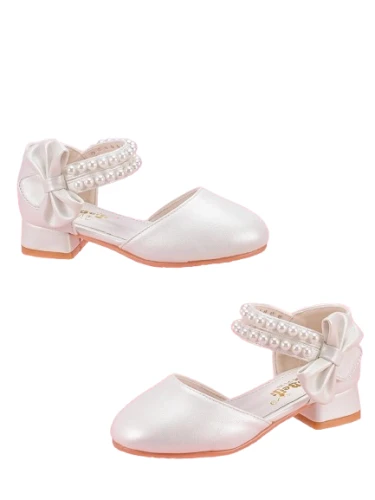 Białe perłowe pantofelki komunijne dla dziewczynki z ozdobnymi paskami z perełek oraz dużą kokardą na pięcie.
