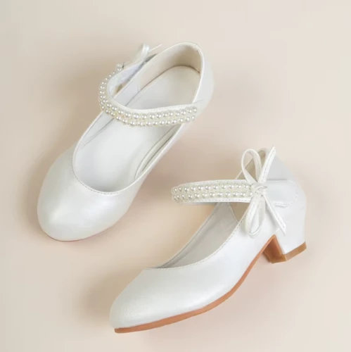 Eleganckie białe pantofelki komunijne dla dziewczynki z perłowym połyskiem, paskami z perełek i ozdobną kokardą.
