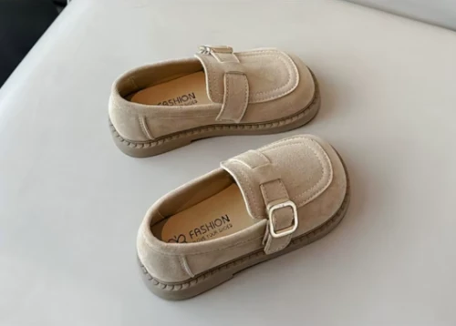 Zamszowe mokasyny dla dziewczynki z ozdobnym paskiem i prostym złotym elementem, dostępne w kolorze brązowym i beżowym.