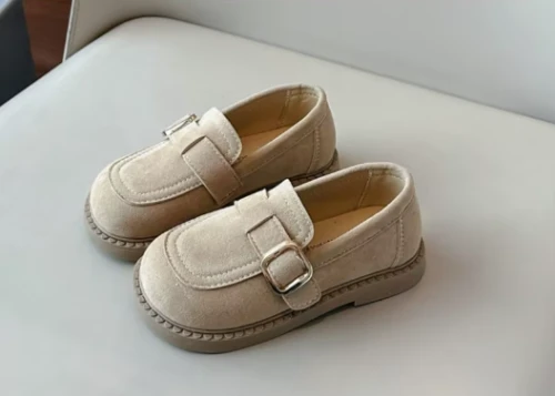 Zamszowe mokasyny dla dziewczynki z ozdobnym paskiem i prostym złotym elementem, dostępne w kolorze brązowym i beżowym.