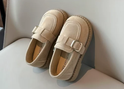 Zamszowe mokasyny dla dziewczynki z ozdobnym paskiem i prostym złotym elementem, dostępne w kolorze brązowym i beżowym.