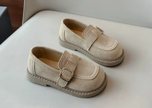 Zamszowe mokasyny dla dziewczynki z ozdobnym paskiem i prostym złotym elementem, dostępne w kolorze brązowym i beżowym.