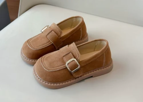 Zamszowe mokasyny dla dziewczynki z ozdobnym paskiem i prostym złotym elementem, dostępne w kolorze brązowym i beżowym.